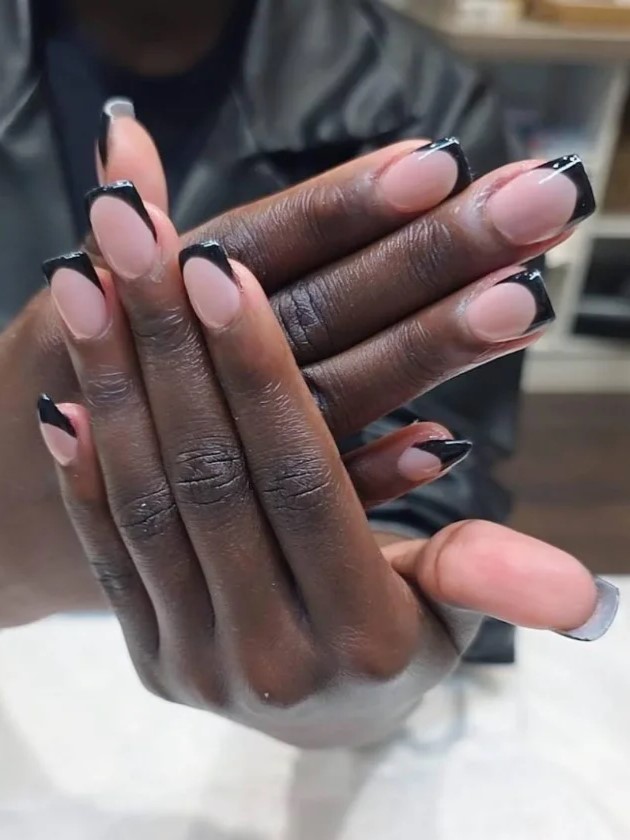 Femme dans un salon donglerie montrant sa manucure BIAB nude avec des extensions noires à lappareil photo