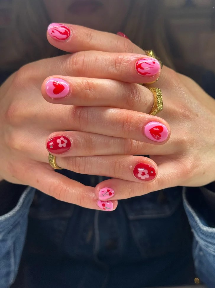 Mains jointes dune femme avec une manucure BIAB rose vif et rouge avec du nail art