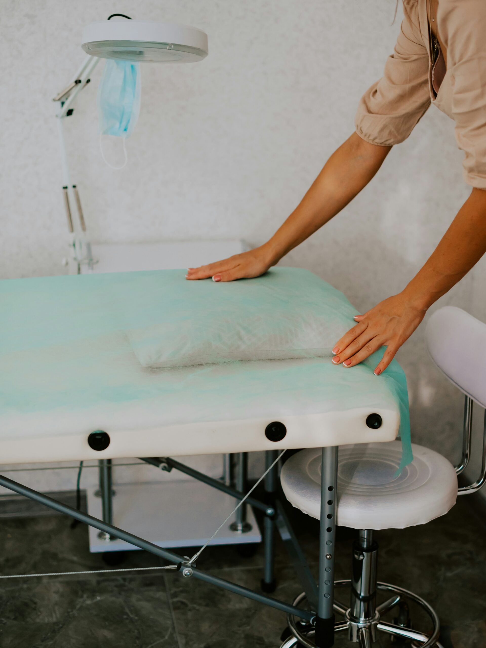 Une cabine de soin esthétique propre et hygiénique, avec une technicienne disposant une feuille de protection sur le lit de soin