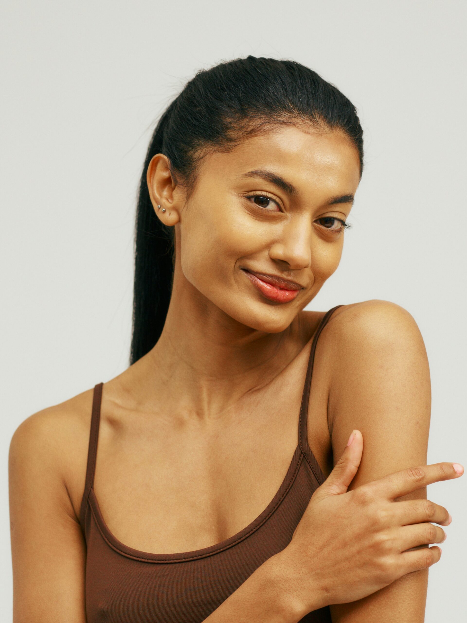 Portrait d’une jeune femme portant un débardeur à bretelles, souriante, caressant ses bras lisses