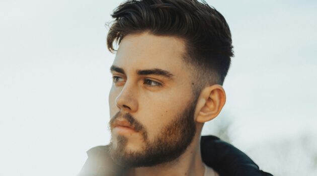 Homme debout en extérieur avec des cheveux foncés portant un taper fade et un dessus texturé