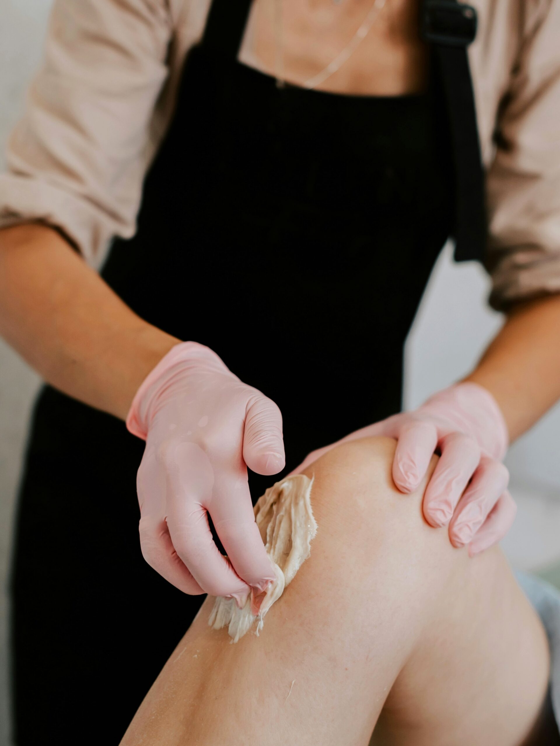Vue de profil d’une esthéticienne appliquant de la cire sur la jambe d’une cliente allongée confortablement sur une table de soin en institut