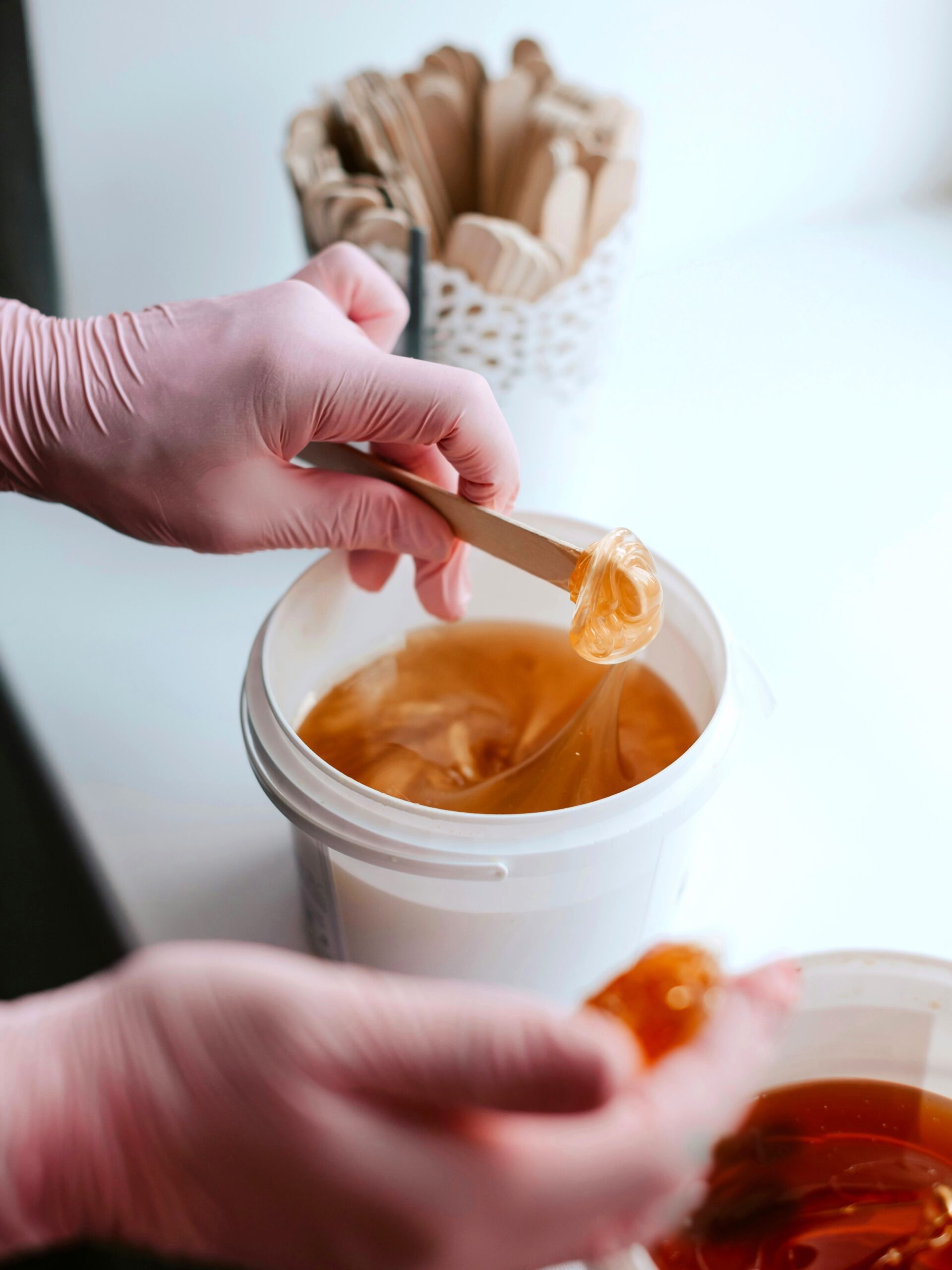 Gros plan sur deux pots de cire au sucre avec une esthéticienne prélevant de la cire à l’aide d’une spatule