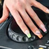 Une main arborant l’electric mani posée sur le jog wheel d’une platine DJ Pioneer, avec des french tips fluo en imprimé animalier et en volutes