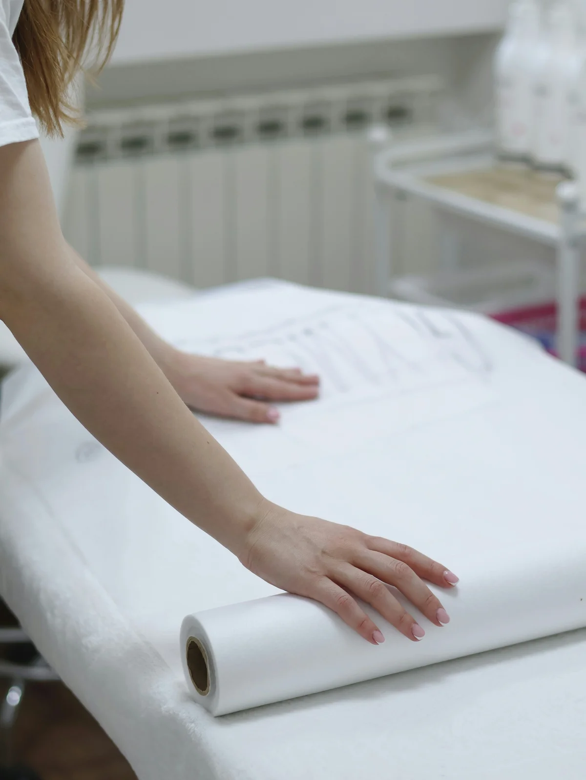 Gros plan sur les bras d'une esthéticienne déroulant une feuille de papier propre sur une table de soin pour préparer un traitement