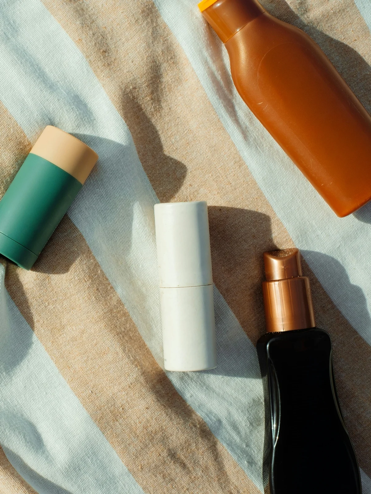 Vue de dessus de petits flacons et tubes de produits de soin posés sur un tissu de coton rayé