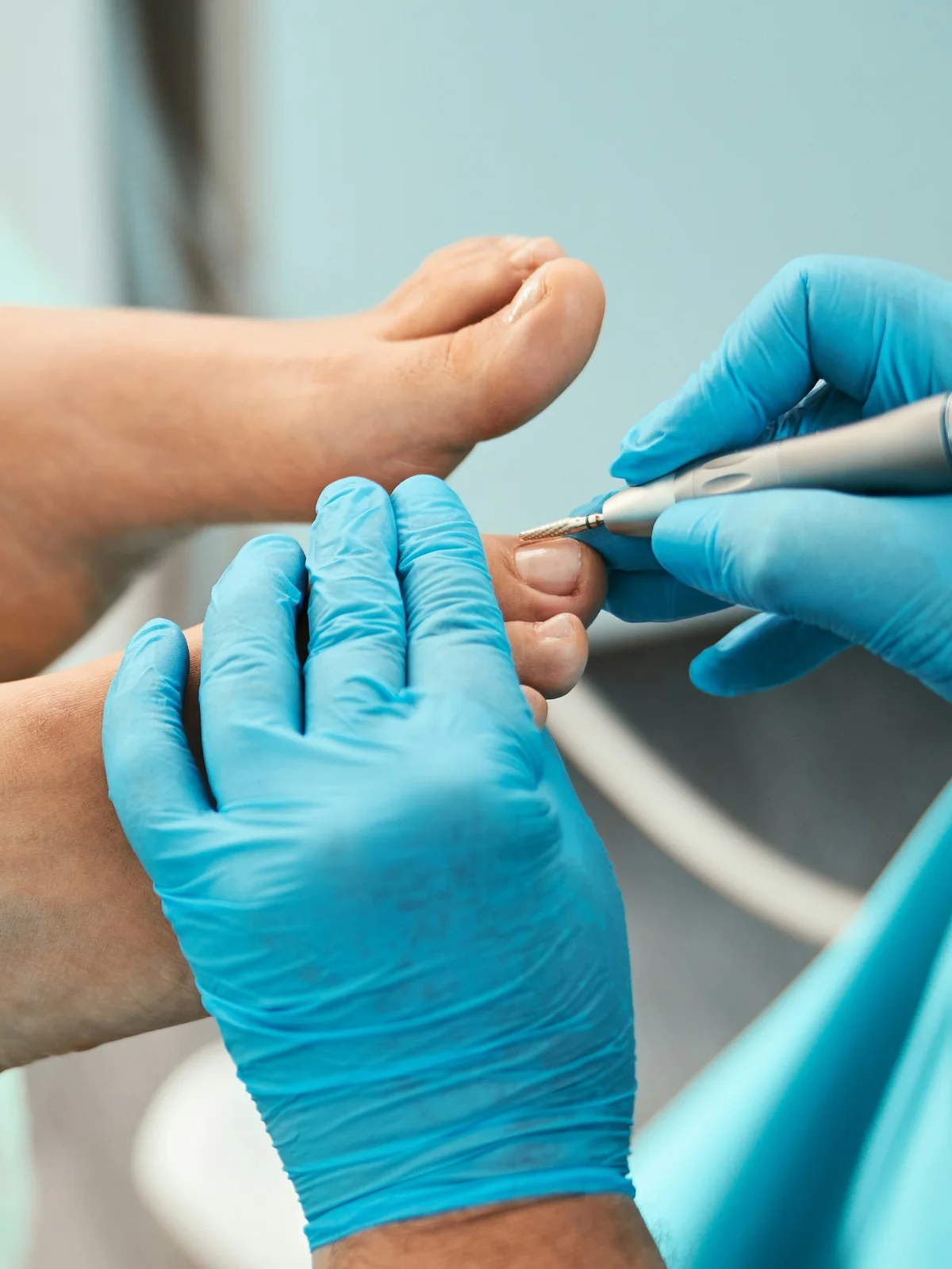 Gros plan sur une esthéticienne gantée qui nettoie les cuticules des orteils d'une cliente avec un petit instrument