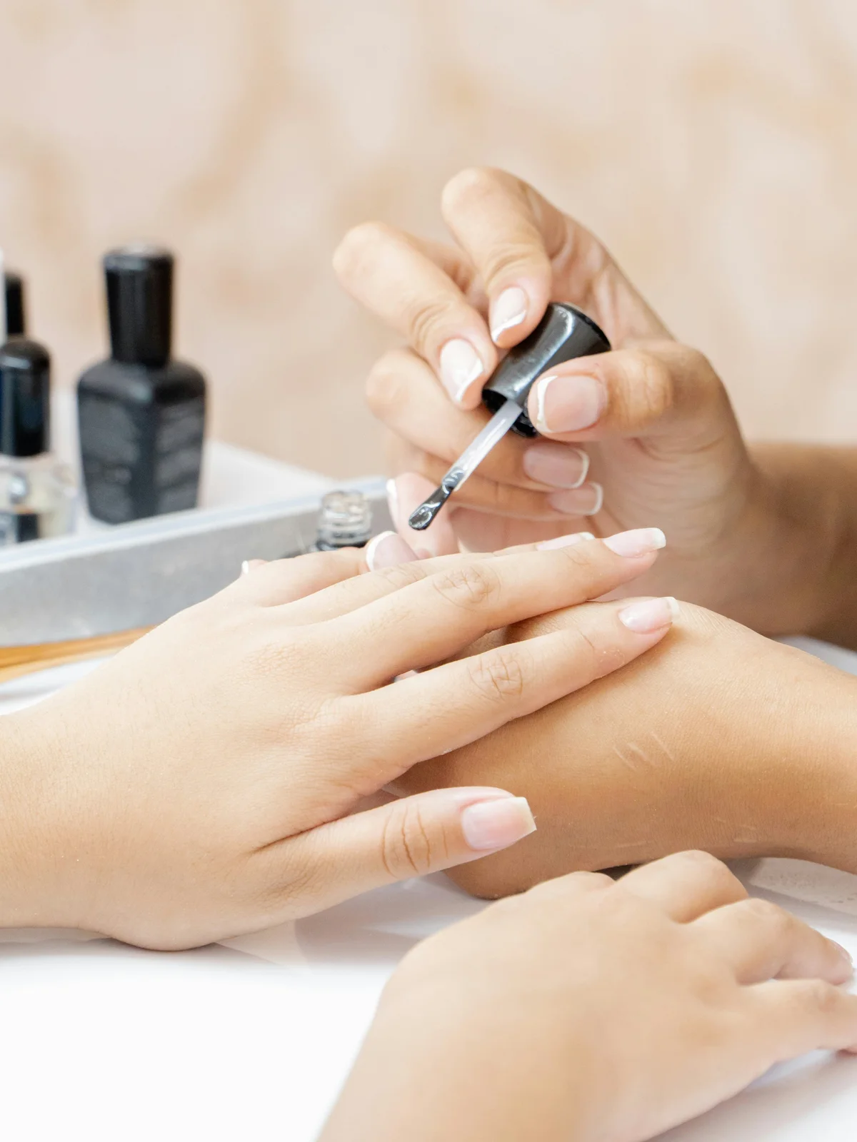 Gros plan sur une prothésiste qui applique un soin fortifiant transparent sur les ongles d'une cliente en salon