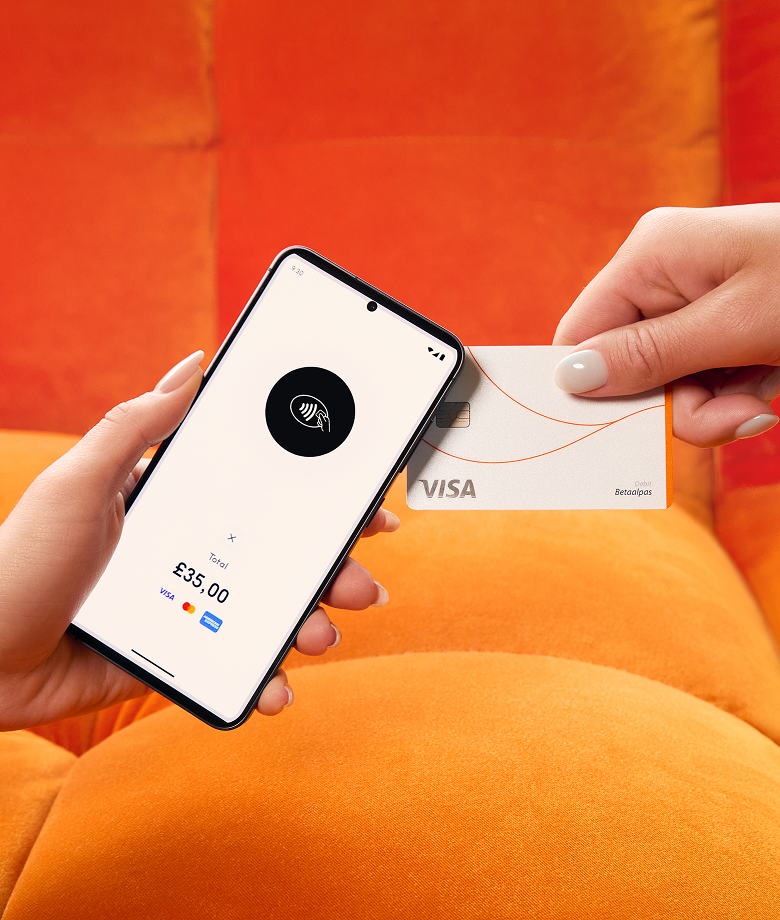Una mano tiene uno smartphone che funziona come lettore di carte, mostrando un'icona di pagamento contactless e un totale di 35,00 sterline, mentre un'altra mano avvicina una carta di credito Visa bianca per effettuare il pagamento. Lo sfondo è un divano arancione acceso.