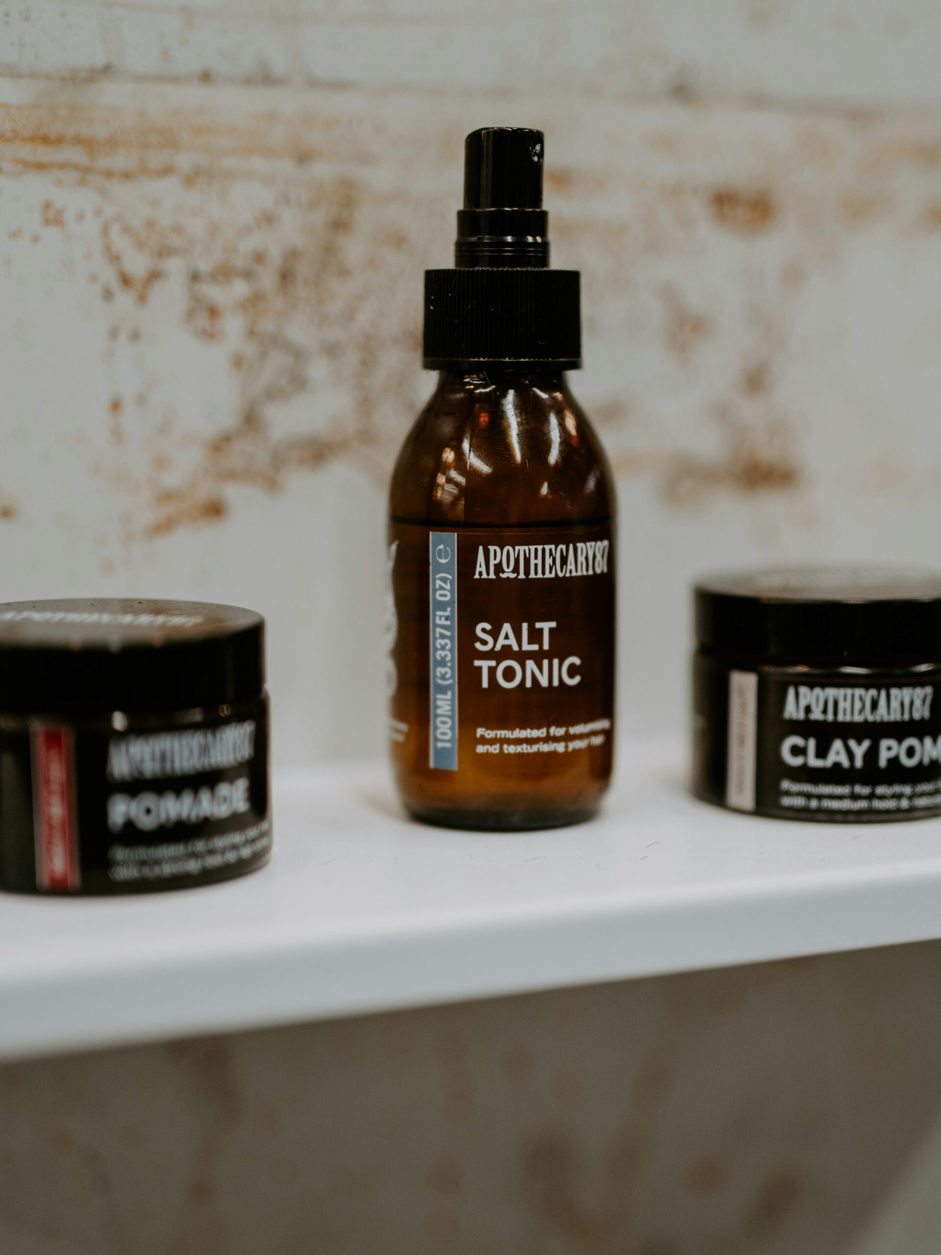 Una serie di prodotti per lo styling del mullet in contenitori marroni su una mensola bianca.
