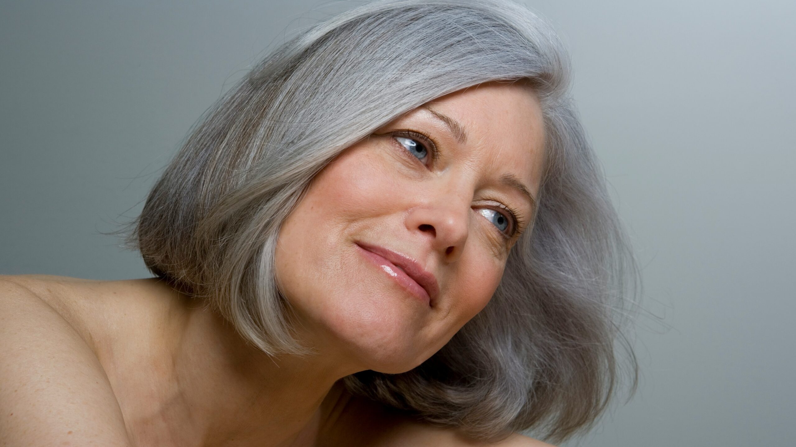 Primo piano di una donna con un caschetto grigio liscio e trucco naturale