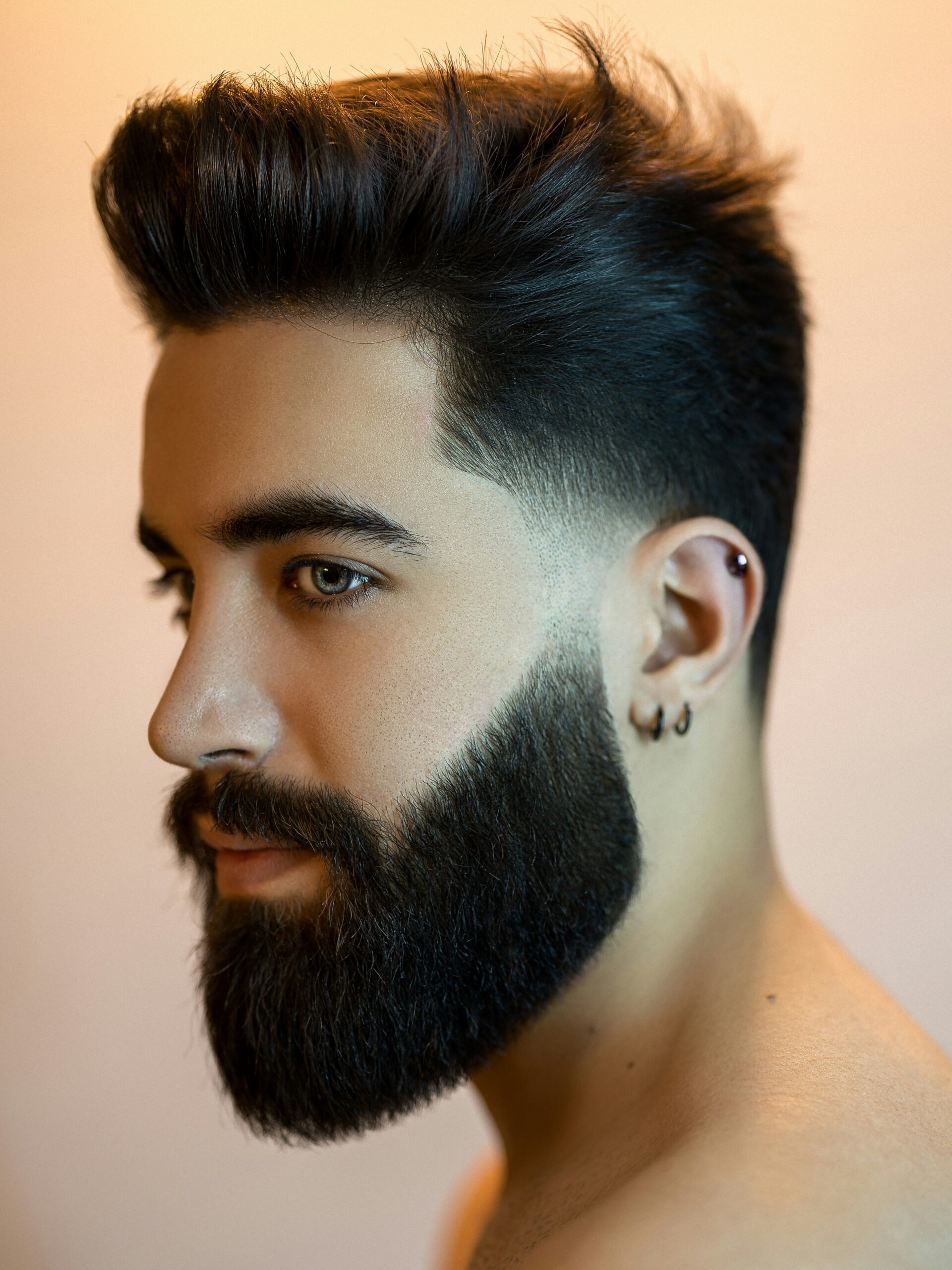 Uomo con viso ovale e capelli scuri, con un taper fade basso voluminoso e la barba