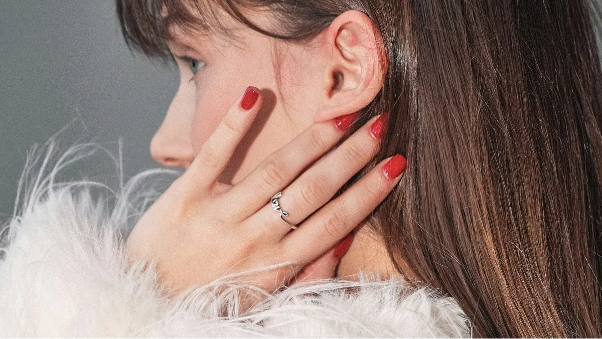 Vista laterale ravvicinata della testa di una donna castana, con la mano appoggiata al viso che mostra una manicure in gel rossa e lucida