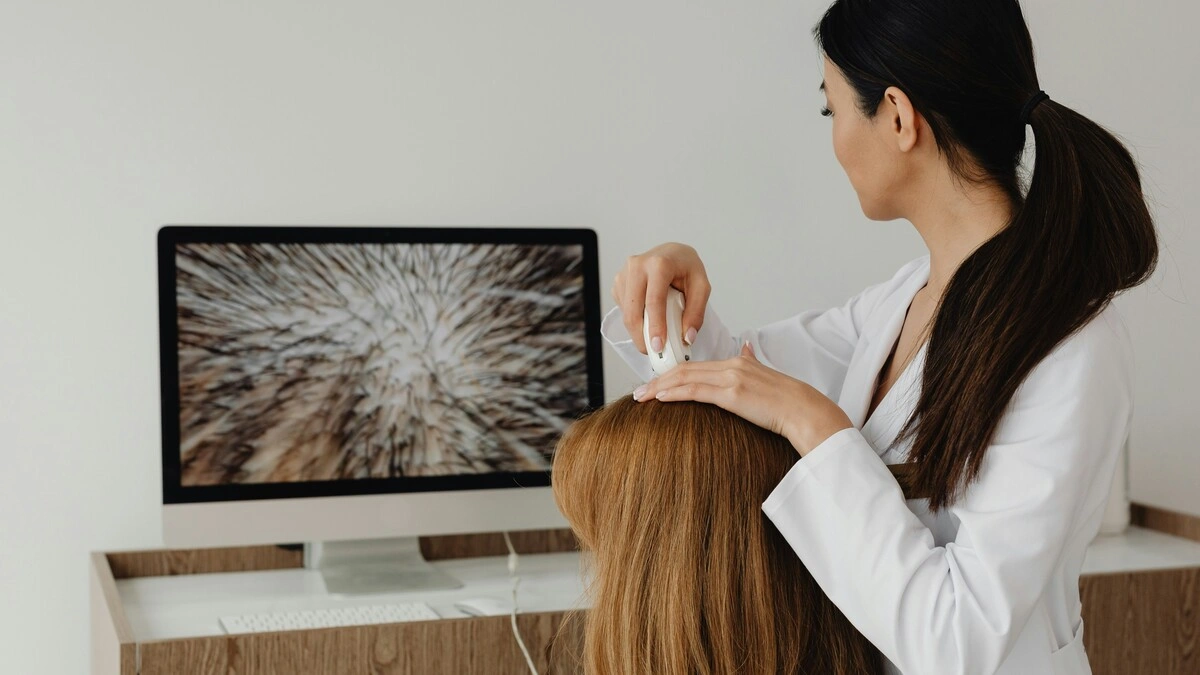 Un professionista osserva il cuoio capelluto di una cliente con una telecamera ad alta risoluzione e mostra l'immagine su un grande schermo