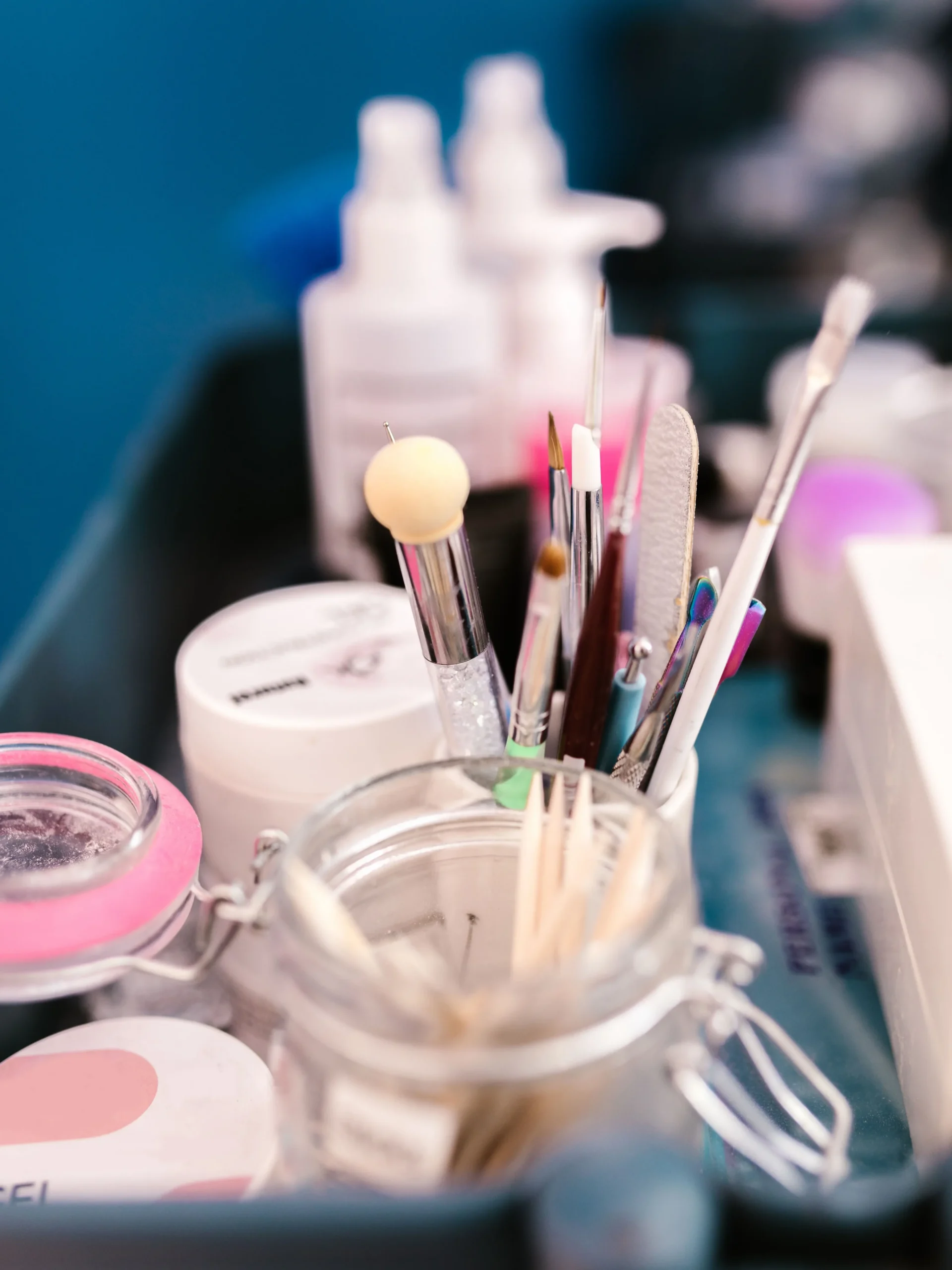 Primo piano della postazione di lavoro di un’onicotecnica in salone, con strumenti per manicure, pennelli e prodotti