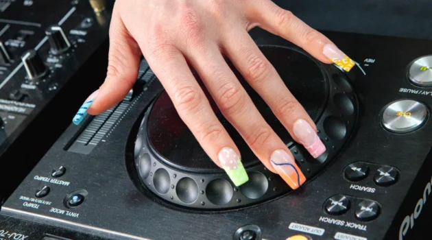 Una mano con l’electric mani appoggiata sul jog wheel di un lettore DJ Pioneer, con french tip al neon in stampa animalier e a spirale