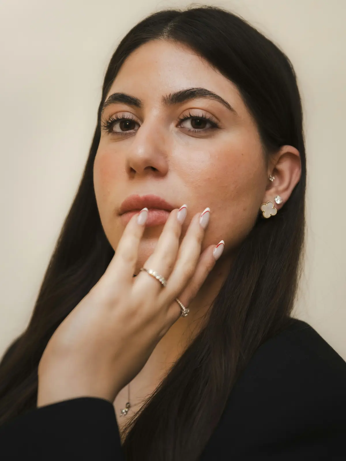 Foto in studio di una donna con piercing al lobo e al tragus che porta una mano curata al viso