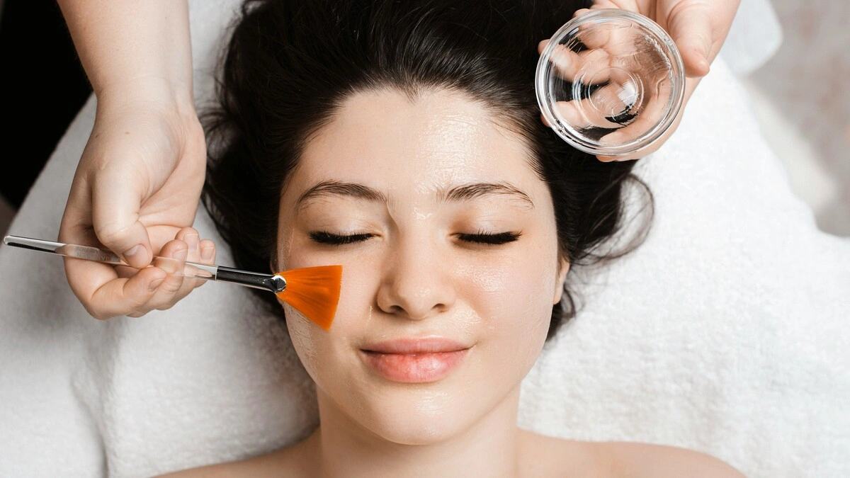 Veduta dall'alto di un'estetista che applica una soluzione di peeling chimico sul viso di una cliente con un pennello largo e piatto