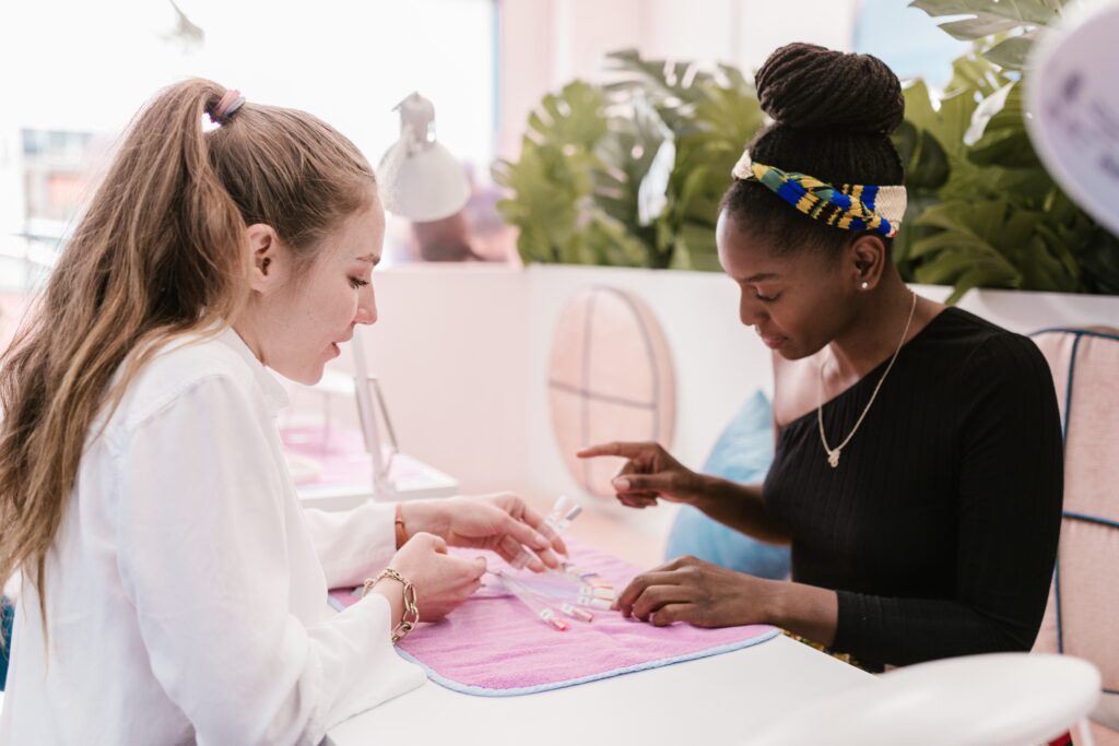 Zwei Frauen suchen eine Nagellackfarbe in einem Nagelstudio aus.