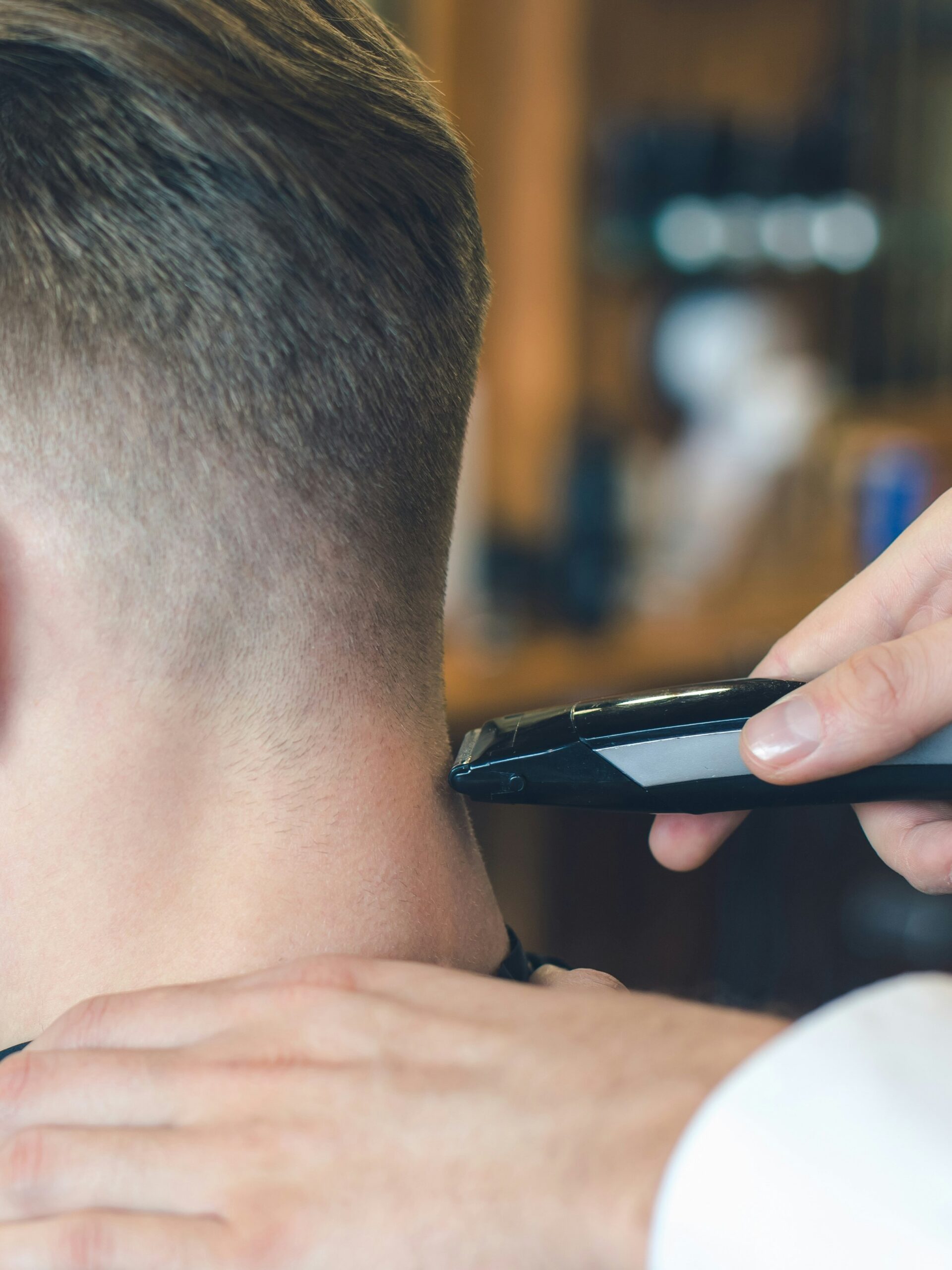 Nahaufnahme eines Barbers, der mit der Haarschneidemaschine einen Taper Fade am Hinterkopf eines Kunden mit glattem Haar schneidet