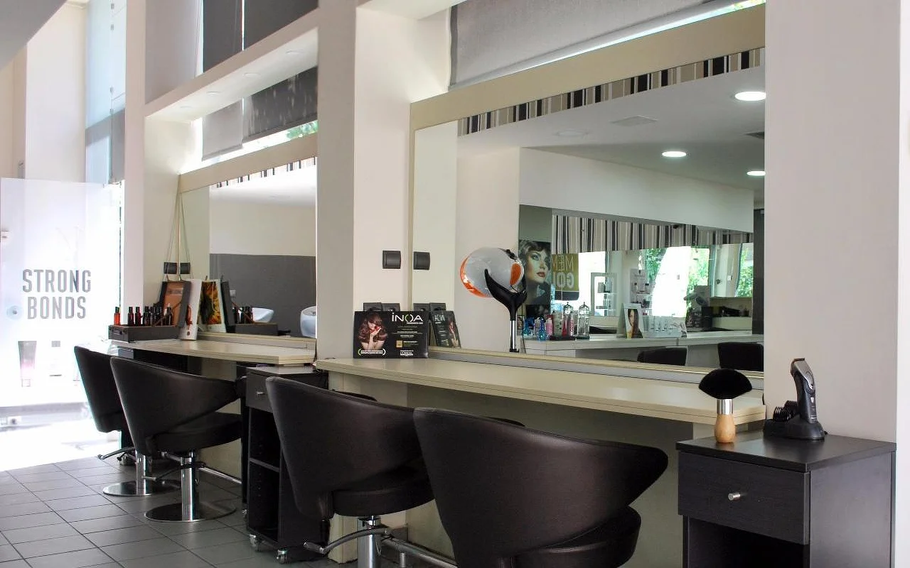 Ein professioneller Friseursalon mit dunklen Leder-Stylingstühlen vor grossen Spiegeln, Haarpflegeprodukten entlang der Theke, hohen Decken und natürlichem Licht durch Oberlichter.