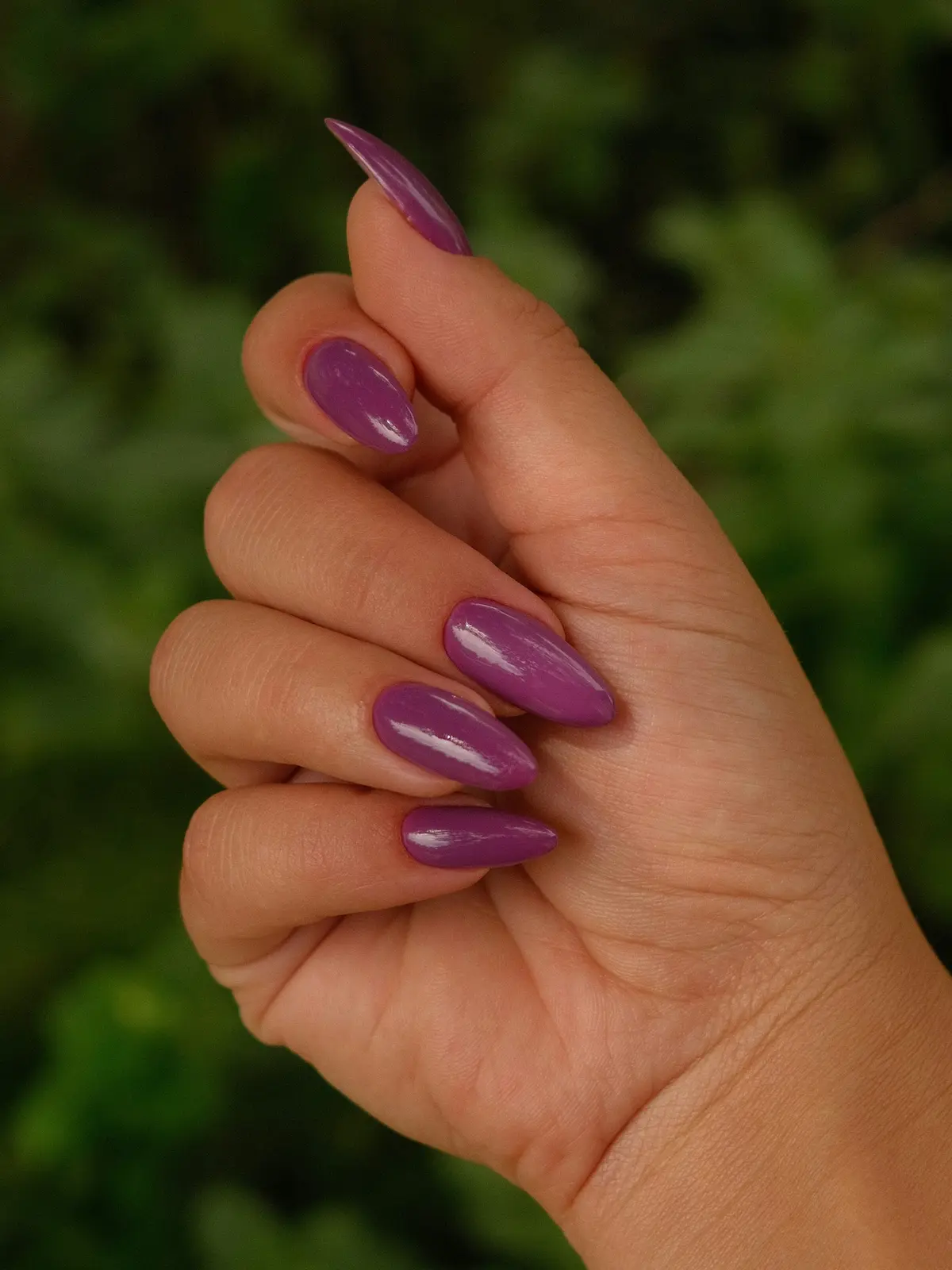 Nahaufnahme der Hand einer Frau mit violetten Acrylnägeln in Mandelform