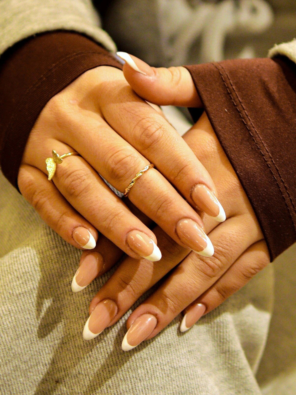 Die Hände einer Frau zeigen eine auffällige French-Tips-Maniküre in einer Kombination aus Beige und Weiss auf langen, mandelförmigen Nägeln