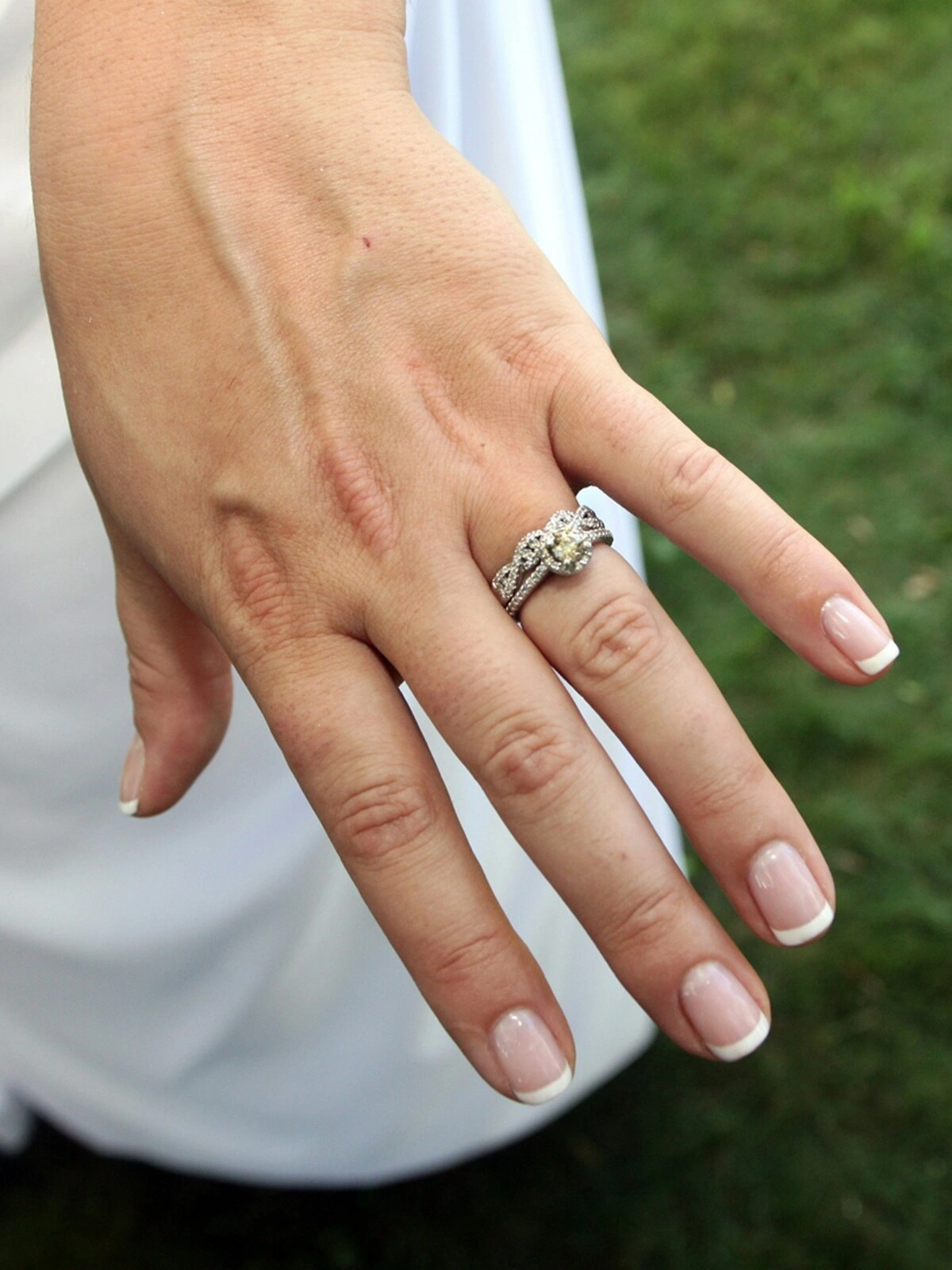Die Hand einer Frau mit einer gepflegten French-Tips-Maniküre in klassischer Kombination aus Nude und Weiss auf kurzen, eckig-ovalen Nägeln