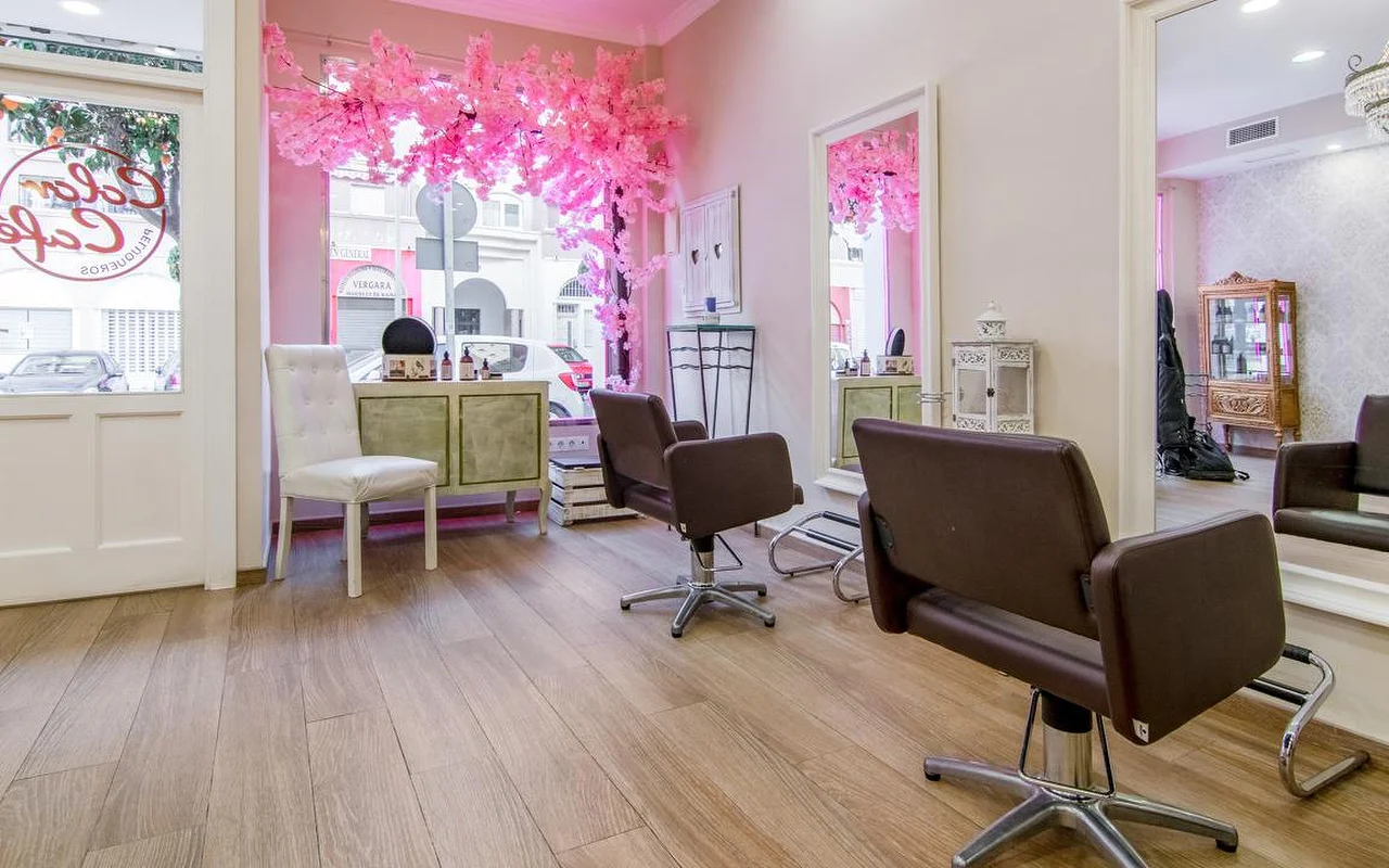 Das Innere von Color Café Peluqueros in Torremolinos, ein Friseursalon mit rosa Wänden, braunen Styling-Stühlen, grossen Spiegeln und einer rosa Kirschblüten-Deko im Schaufenster.