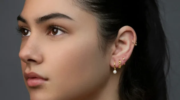 Studioaufnahme einer Frau mit einem Curated Ear aus mehreren Ohrläppchen-Piercings und einem Helix-Ring