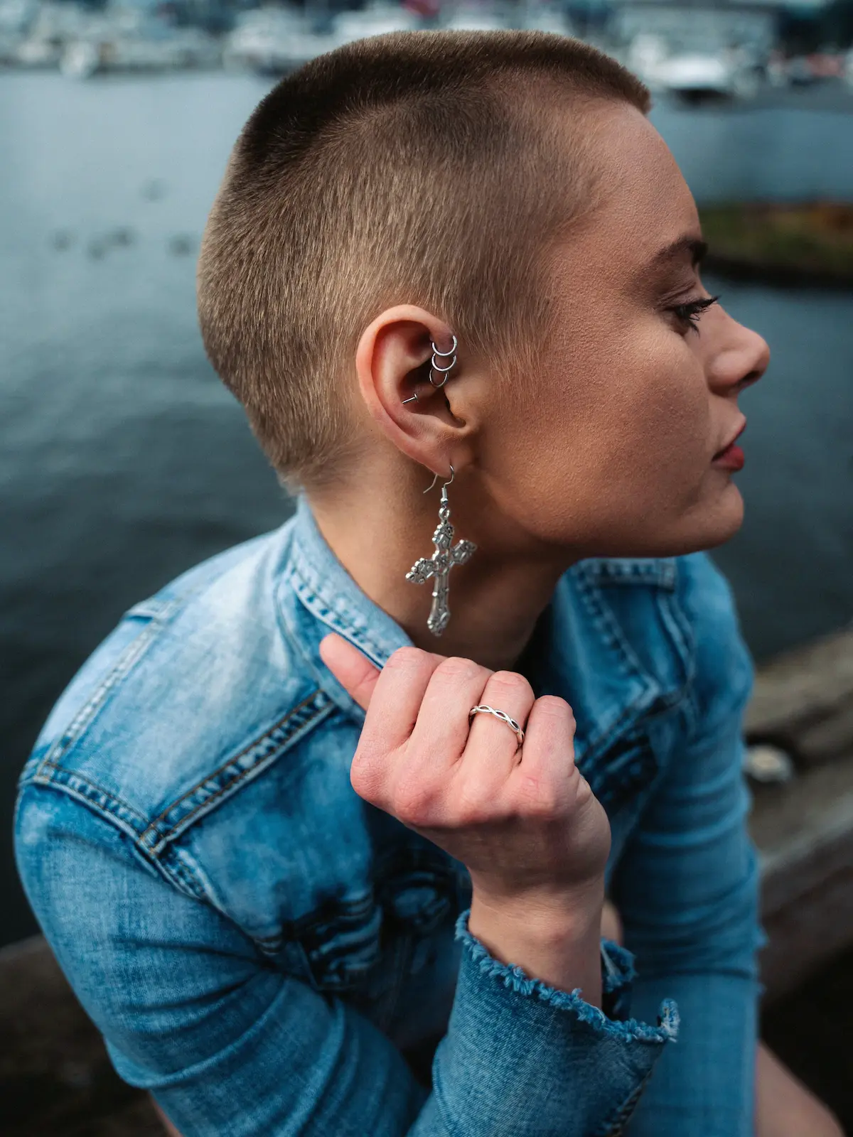Aufnahme von oben: eine Frau mit Forward-Helix-, Helix- und Ohrläppchen-Piercings sitzt an einem Fluss in der Stadt