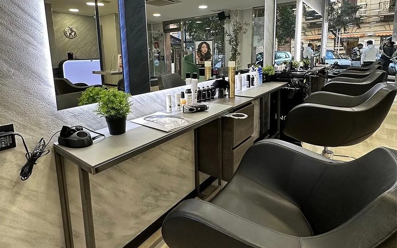 Der Styling-Bereich von Equipe Beauty, mit einer Reihe schwarzer Stühle entlang einer Theke in Marmoroptik, einem grossen hinterleuchteten Spiegel, Styling-Produkten und einer Topfpflanze auf der Theke, und raumhohen Fenstern zur Strasse.