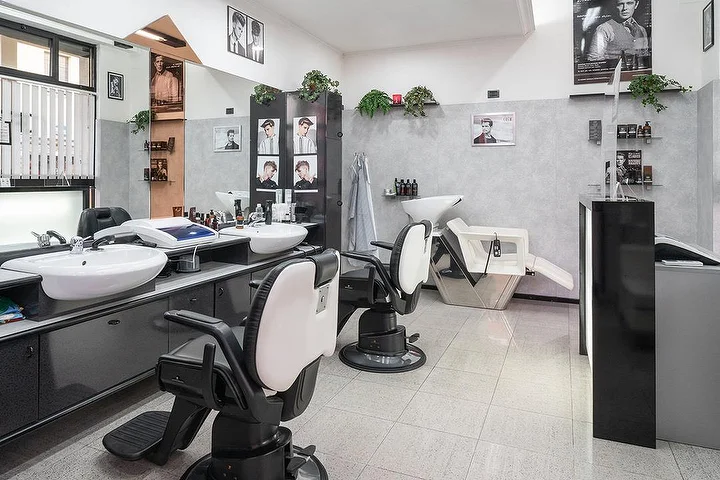 Vintage-Barbier-Stühle und Waschplätze bei Fabio Desole Acconciature Maschili in Sassari mit gerahmten Porträts an den Wänden.