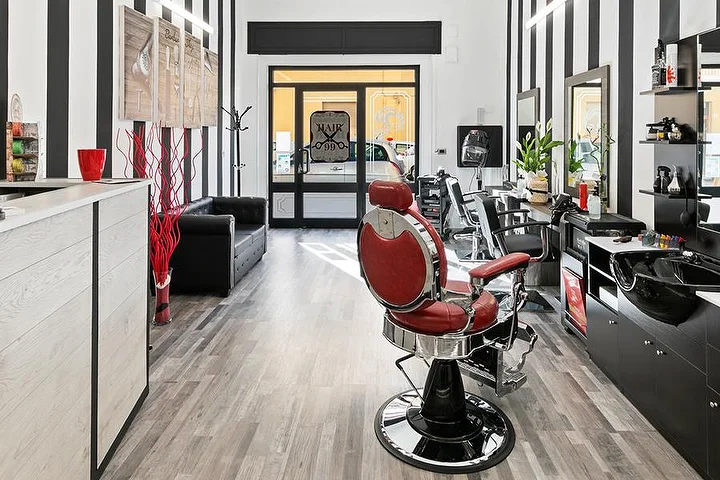 Roter Vintage-Barbier-Stuhl im Hair 99 in Alghero mit den markanten schwarz-weiss gestreiften Wänden.