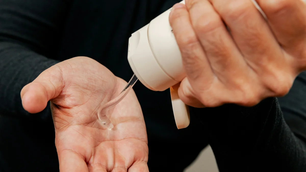 Nahaufnahme der Hände eines Mannes, der mit einer Hand eine weisse Tube Feuchtigkeitsgel in die andere Hand drückt