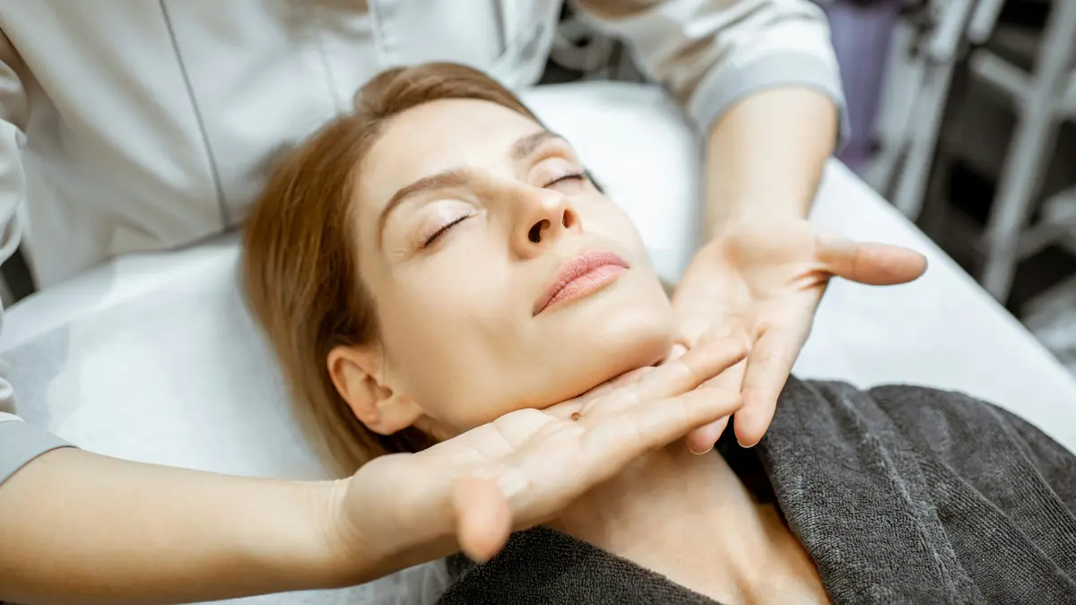 Frau entspannt während einer sanften Lymphdrainage im Gesicht, während die Hände der Fachkraft leicht unter ihrem Kiefer entlanggleiten