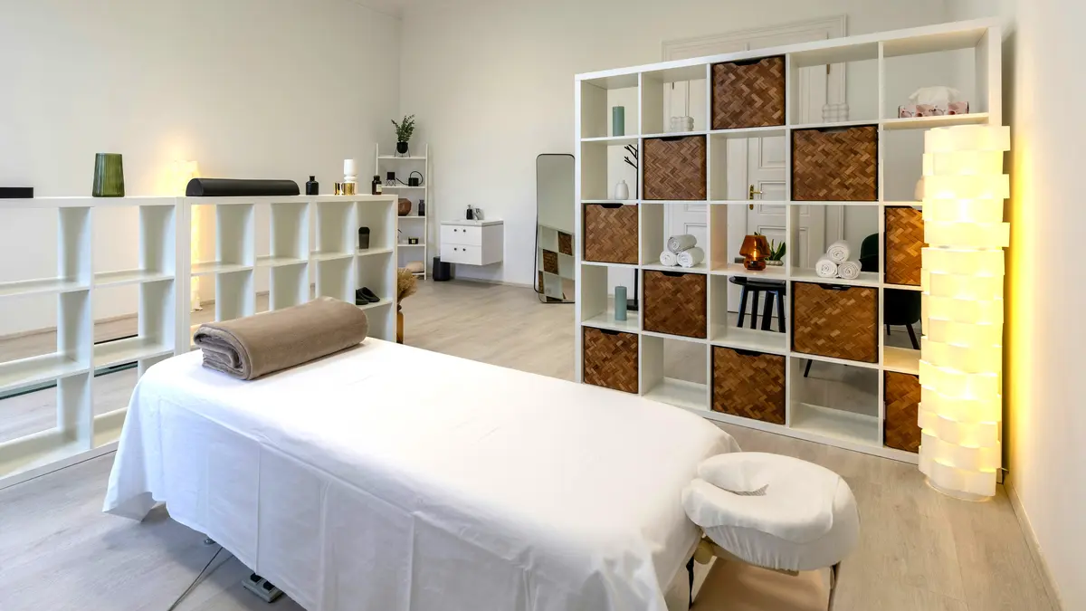 Sauberer, aufgeräumter Behandlungsraum in einem Salon mit frisch bezogener Liege und einer gerollten Decke, bereit für eine Massage